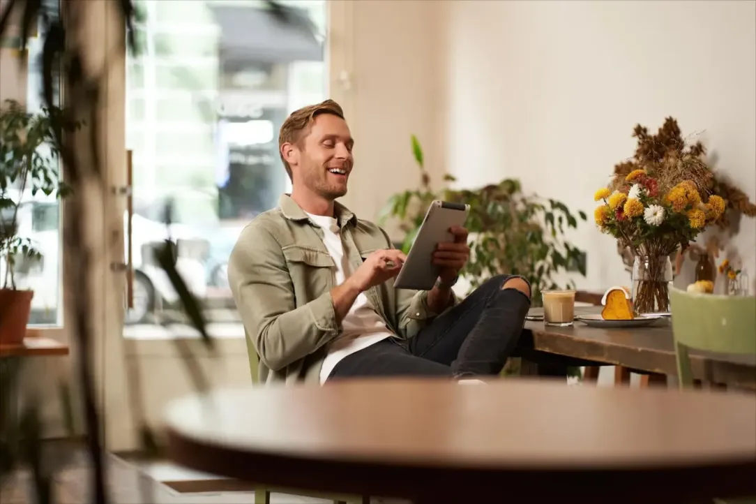 Een man zit aan zijn ontbijt en is online aan het shoppen met de tablet in zijn handen.