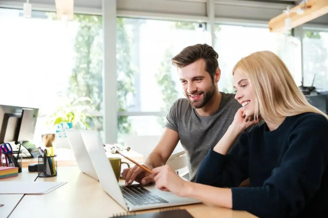 Een man en vrouw vergelijken op hun laptops software in een moderne werkomgeving.